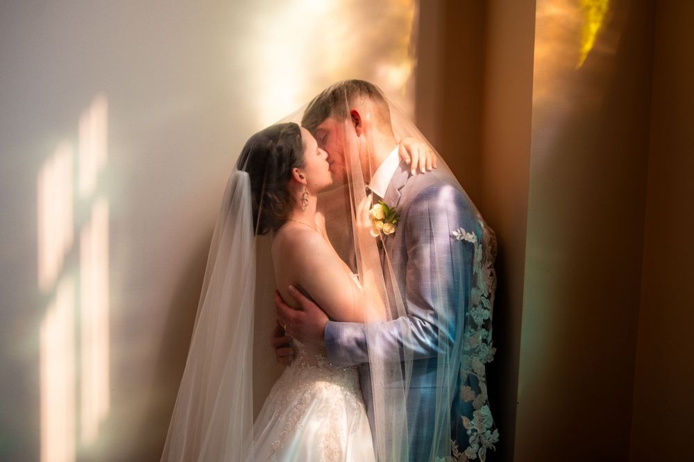 Bride and groom sharing a romantic kiss in soft golden light, bride wearing veil and white gown.