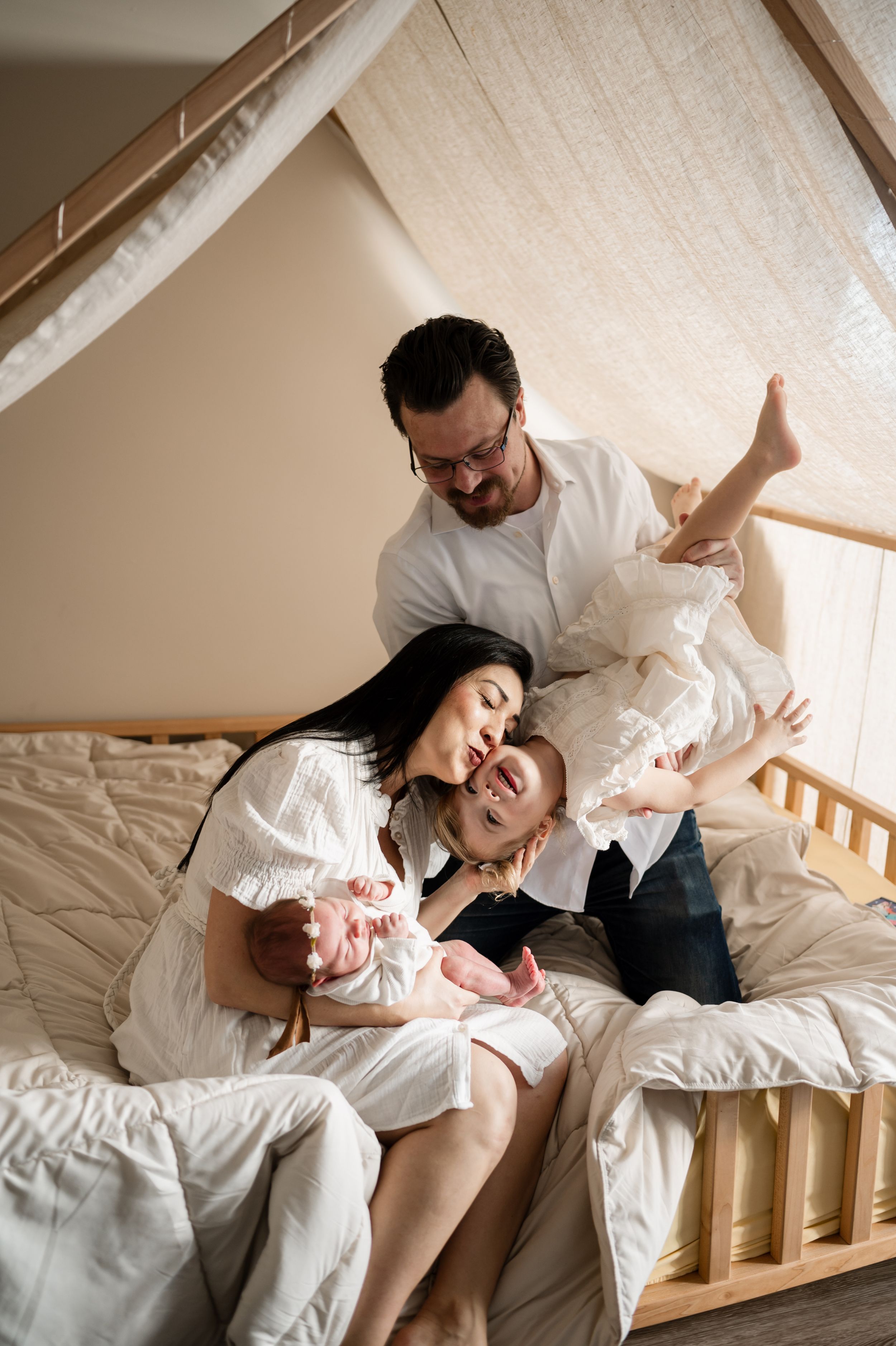 Playful family lifestyle session on white bedding showing joyful interaction and movement.