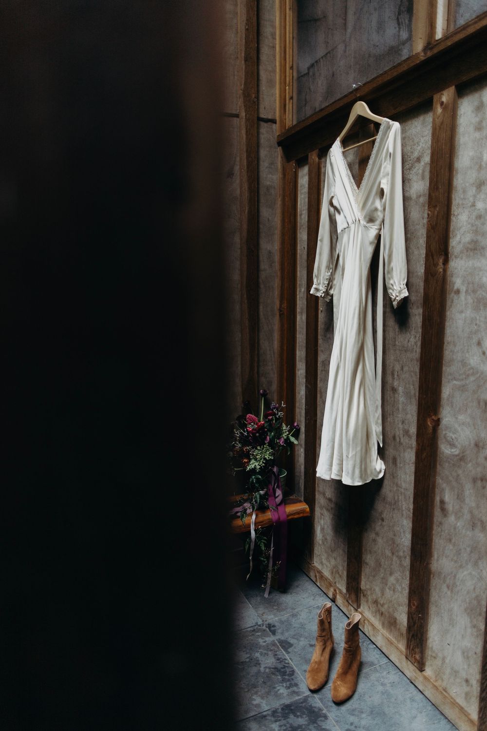 Wedding dress and shoes hanging in rustic wooden room with floral accents.
