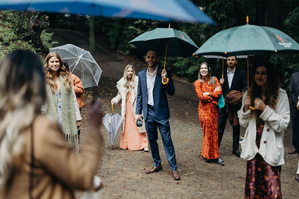 Wedding party walks together holding umbrellas during outdoor celebration.
