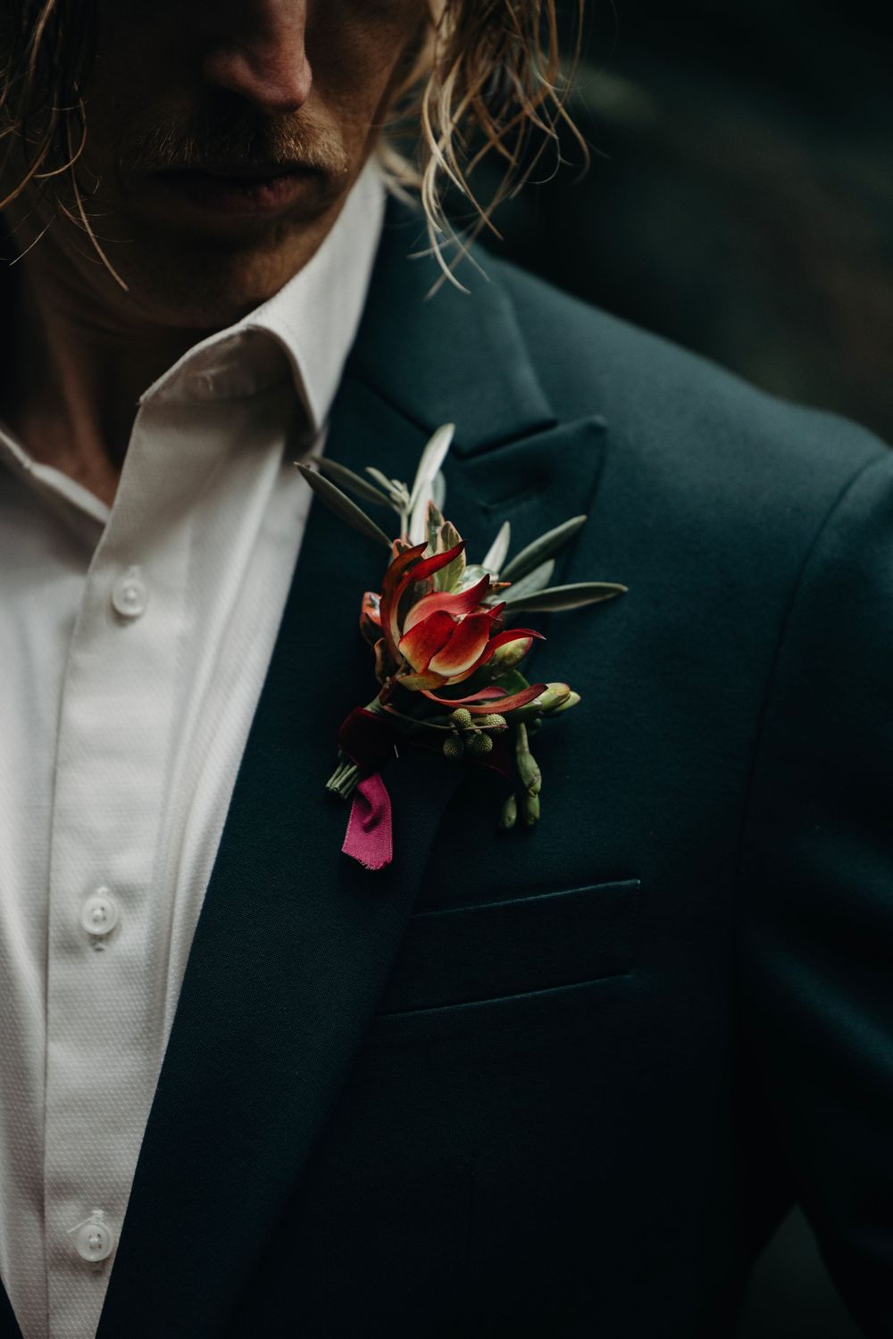 Close-up detail of red floral boutonniere on black suit lapel.