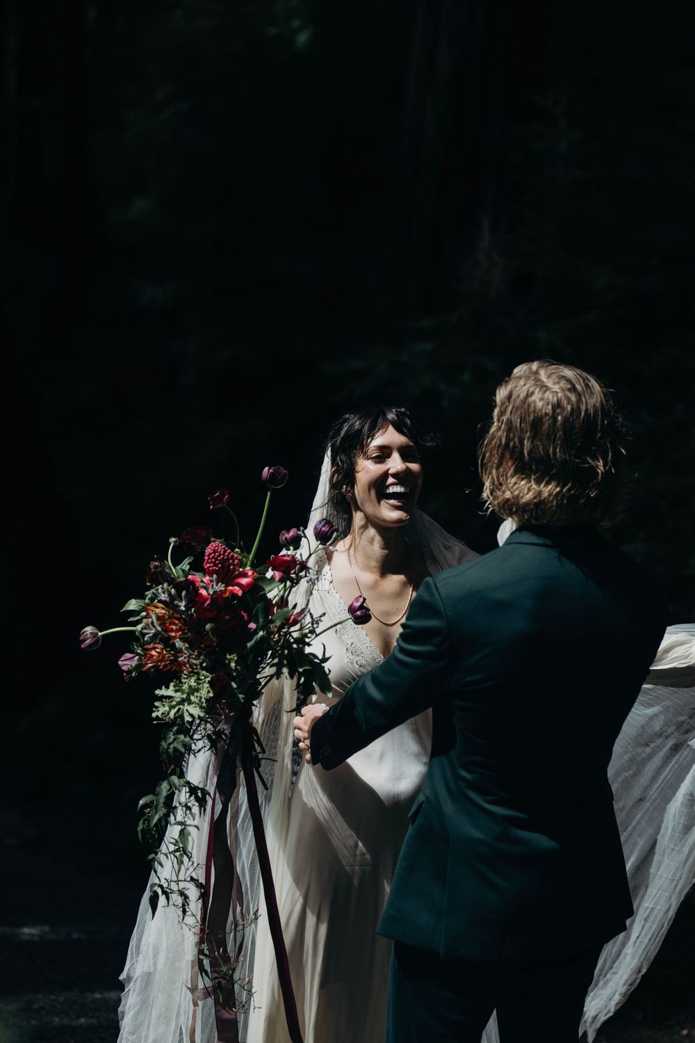 Intimate forest wedding ceremony moment with flowing white veil.