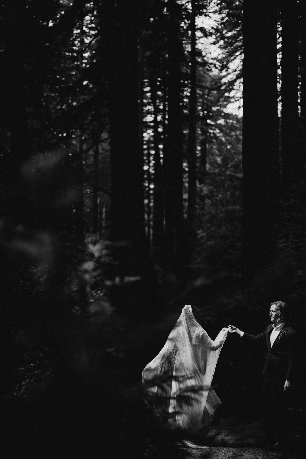 Artistic black and white forest wedding portraits with flowing veil movement.