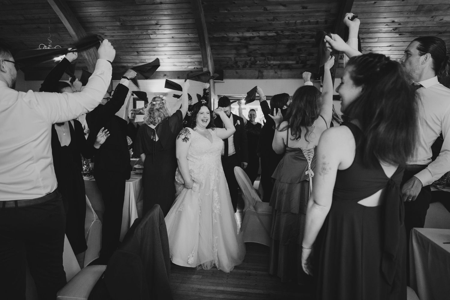 Wedding guests dance together on a dark dance floor at an evening reception celebration.