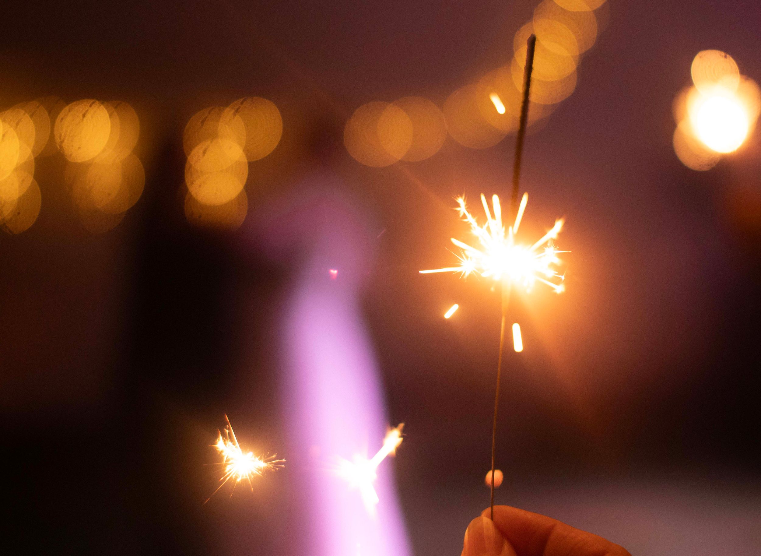Leuchtende Wunderkerze in der Hand mit warmem Bokeh-Lichterhintergrund bei romantischer Hochzeitsfeier