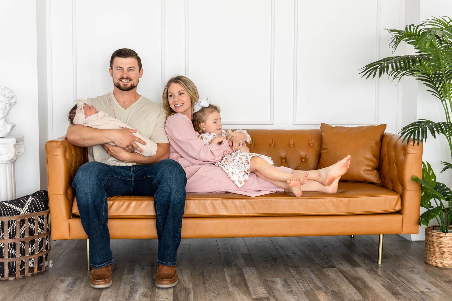 A family sits on a couch admiring their newborn baby.