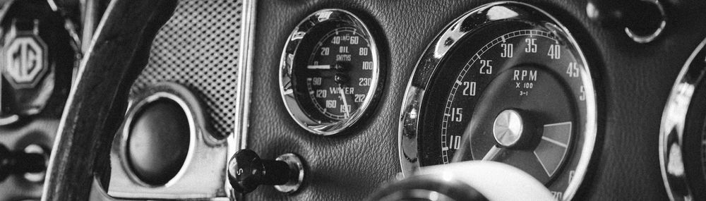 Close-up view of vintage car dashboard showing classic analog gauges and controls in black and chrome finish.
