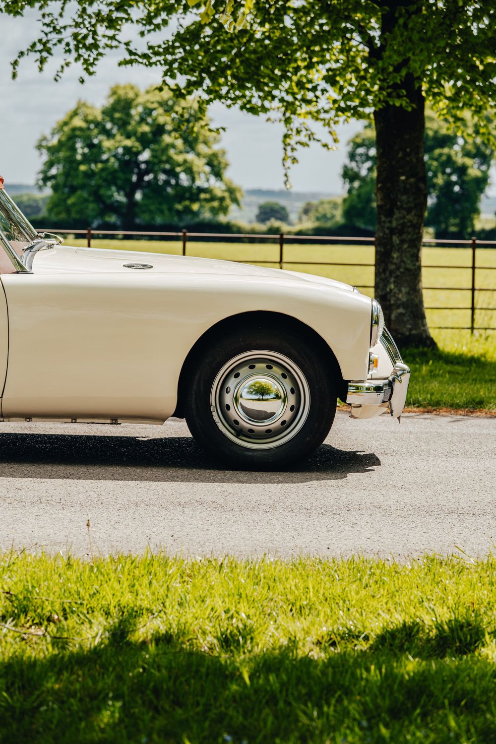 Side view of cream-colored classic MG car wheel and fender against green countryside.
