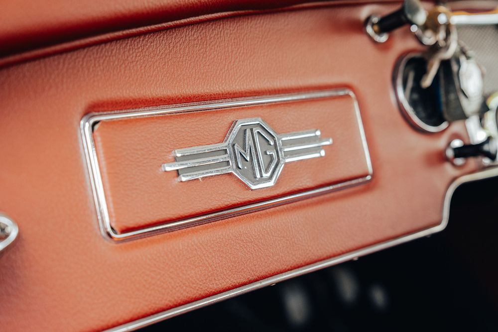 Vintage red leather dashboard interior detail showing MG badging and chrome trim.