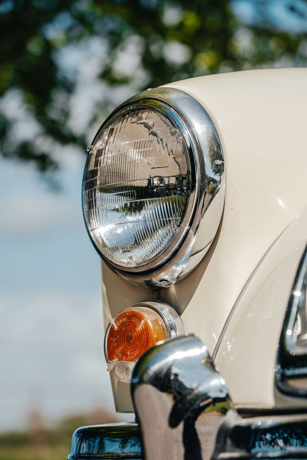 Close-up of chrome headlight and turn signal on classic white MG car.