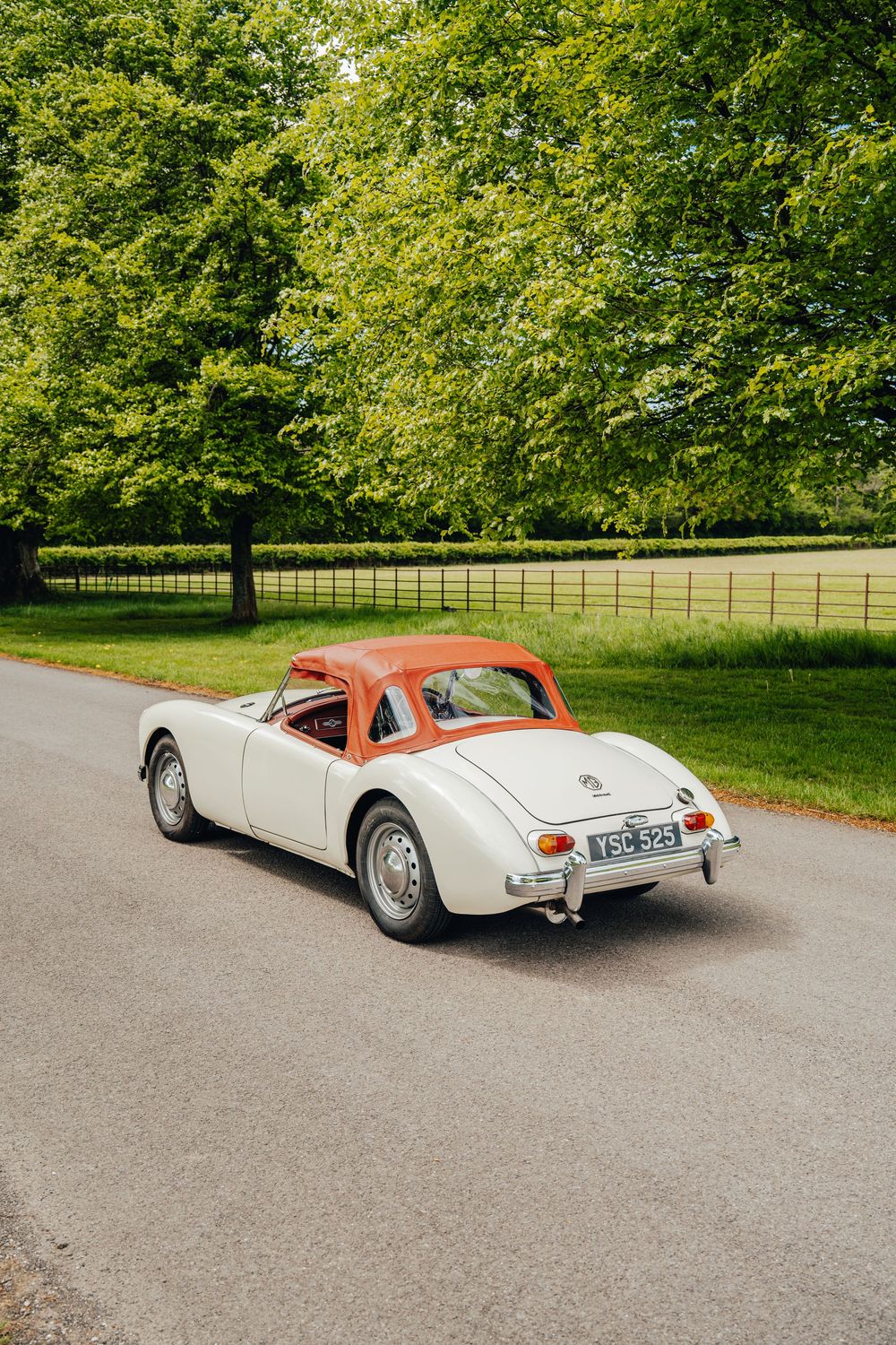 Vintage white MG roadster photographed from multiple angles on a scenic driveway surrounded by green trees.