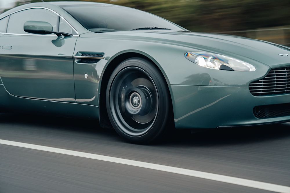 A sleek Aston Martin sports car in motion on a racetrack, showcasing its elegant gray exterior design.