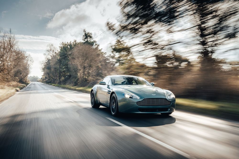 Aston Martin luxury sports car speeding down a rural road with motion blur effect.