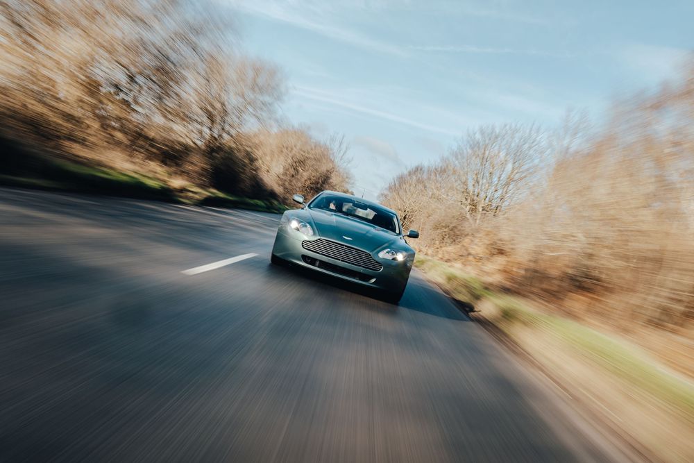 Dynamic shot of a blue Aston Martin driving on a winding road with motion blur.