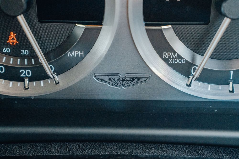 Close-up view of an Aston Martin dashboard showing analog instrument gauges and controls.