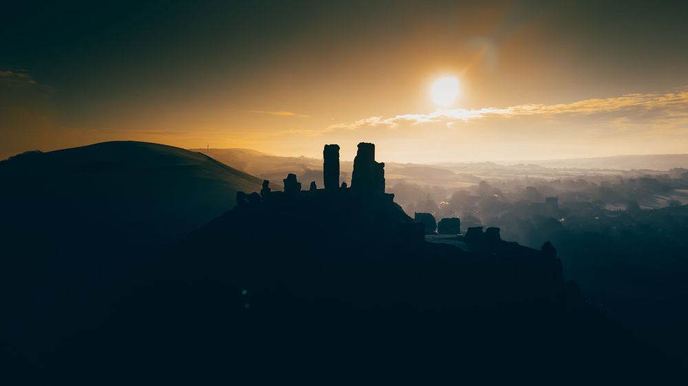 A stunning panoramic view of a mountain range silhouetted against a dramatic sunset sky with golden clouds.