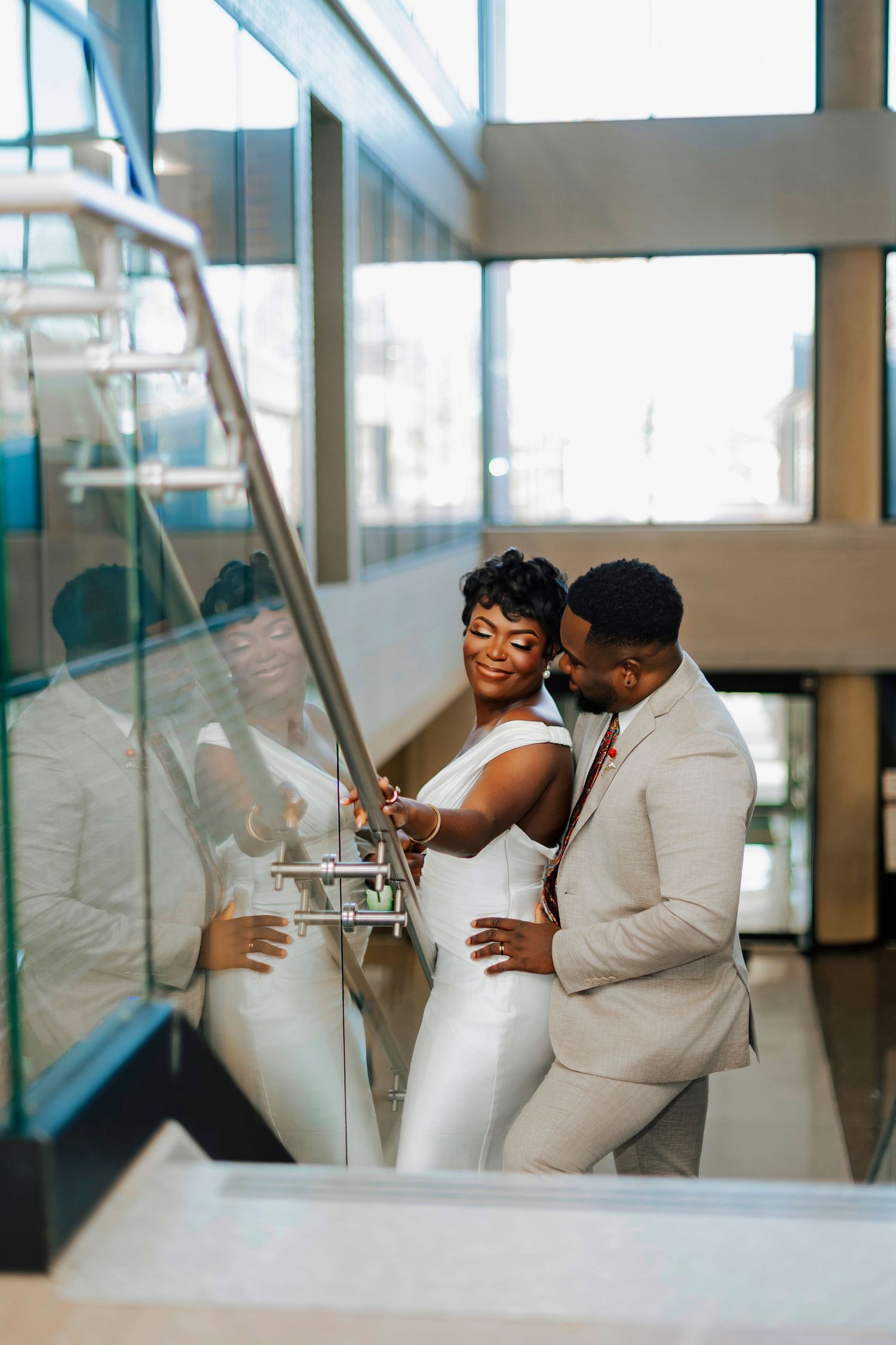 A romantic couple in white outfits share intimate moments in a modern interior space with glass walls.