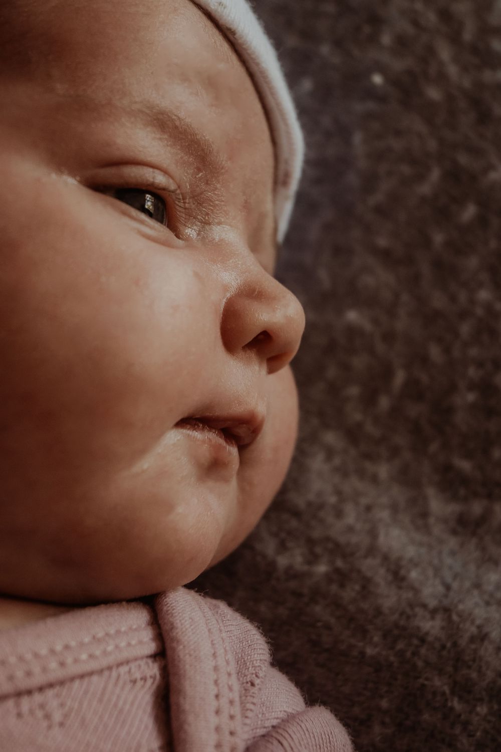 Baby in pink clothing looking to the side with curious expression during a central coast newborn session.