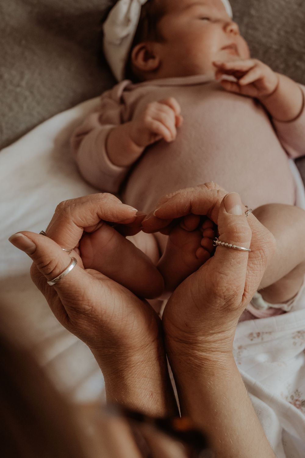 Adult hands gently creating a heart around tiny baby feet against white fabric during a central coast newborn session.