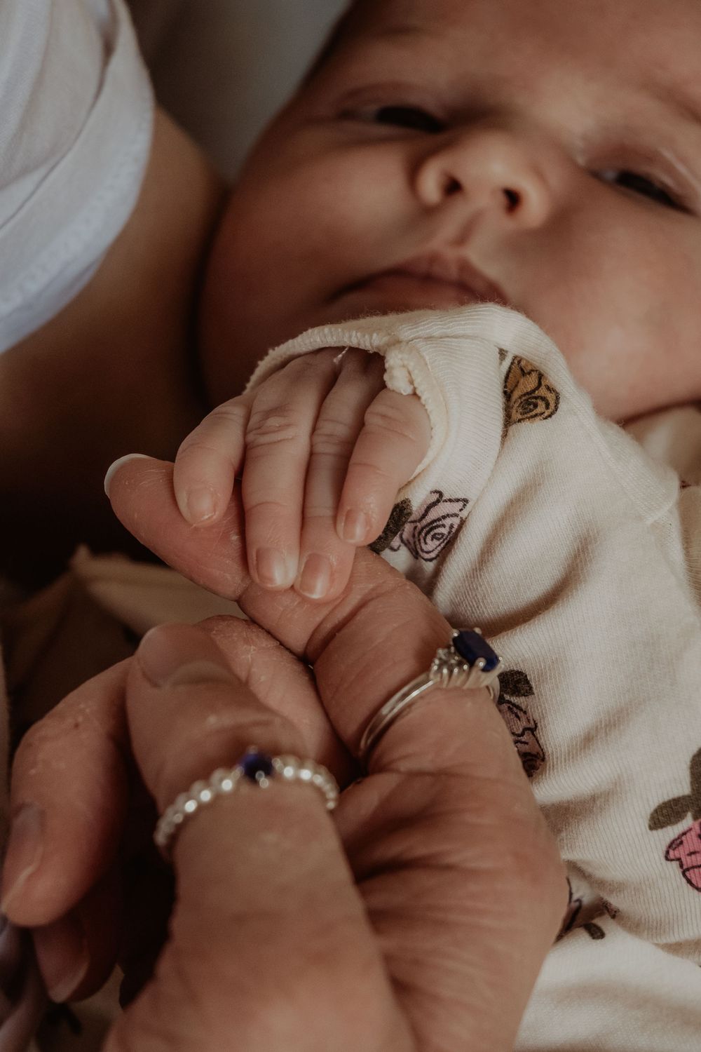 Baby's tiny hand gently held by adult wearing rings against white patterned fabric background at a central coast newborn photoshoot.