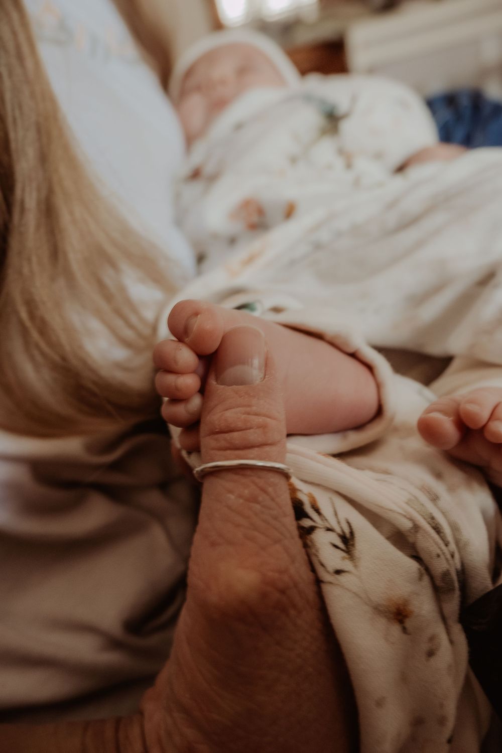 Close-up of adult hand holding baby's tiny foot wrapped in white fabric during a central coast newborn session.