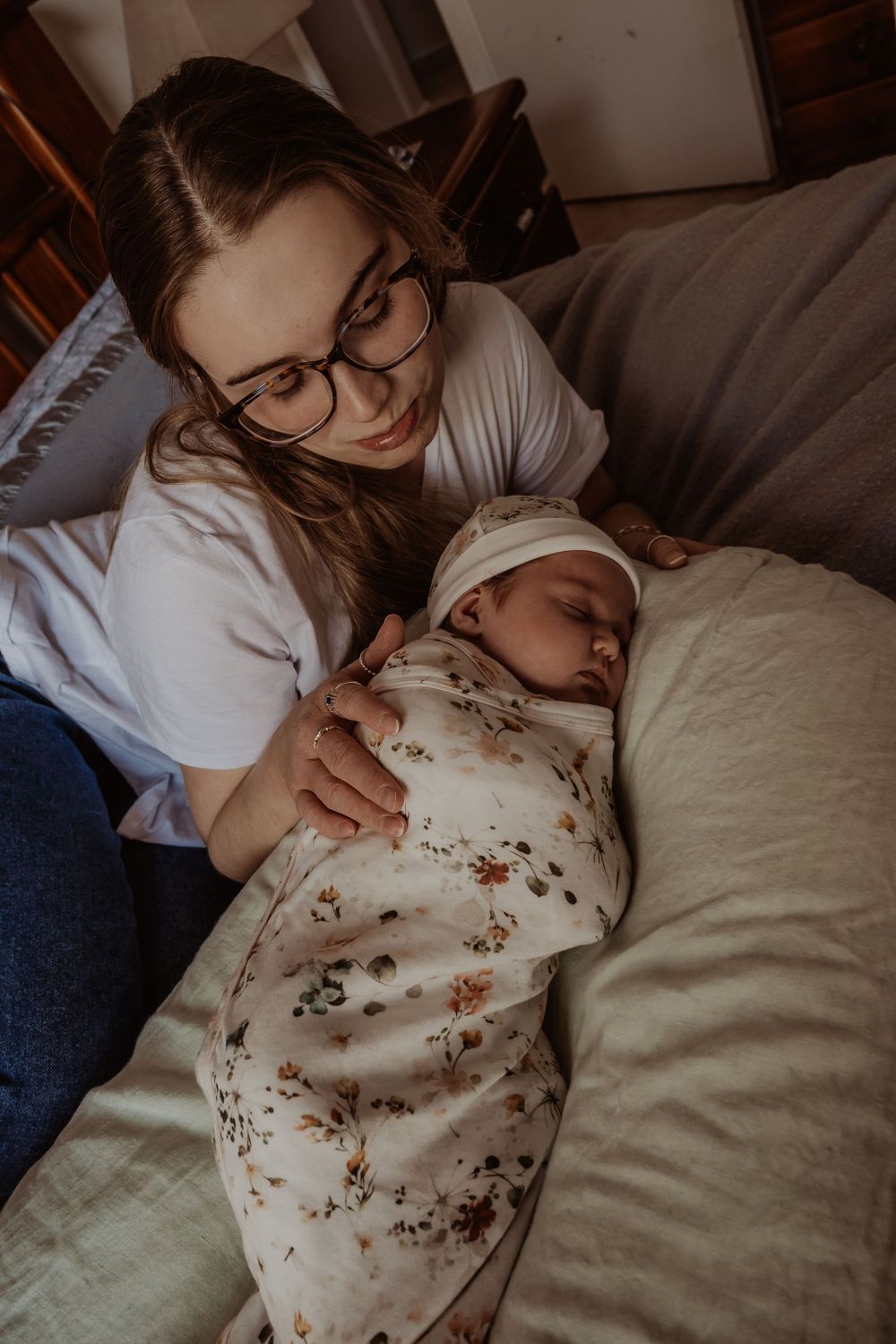 Tender moment between caregiver and sleeping baby on gray couch during a central coast newborn session.