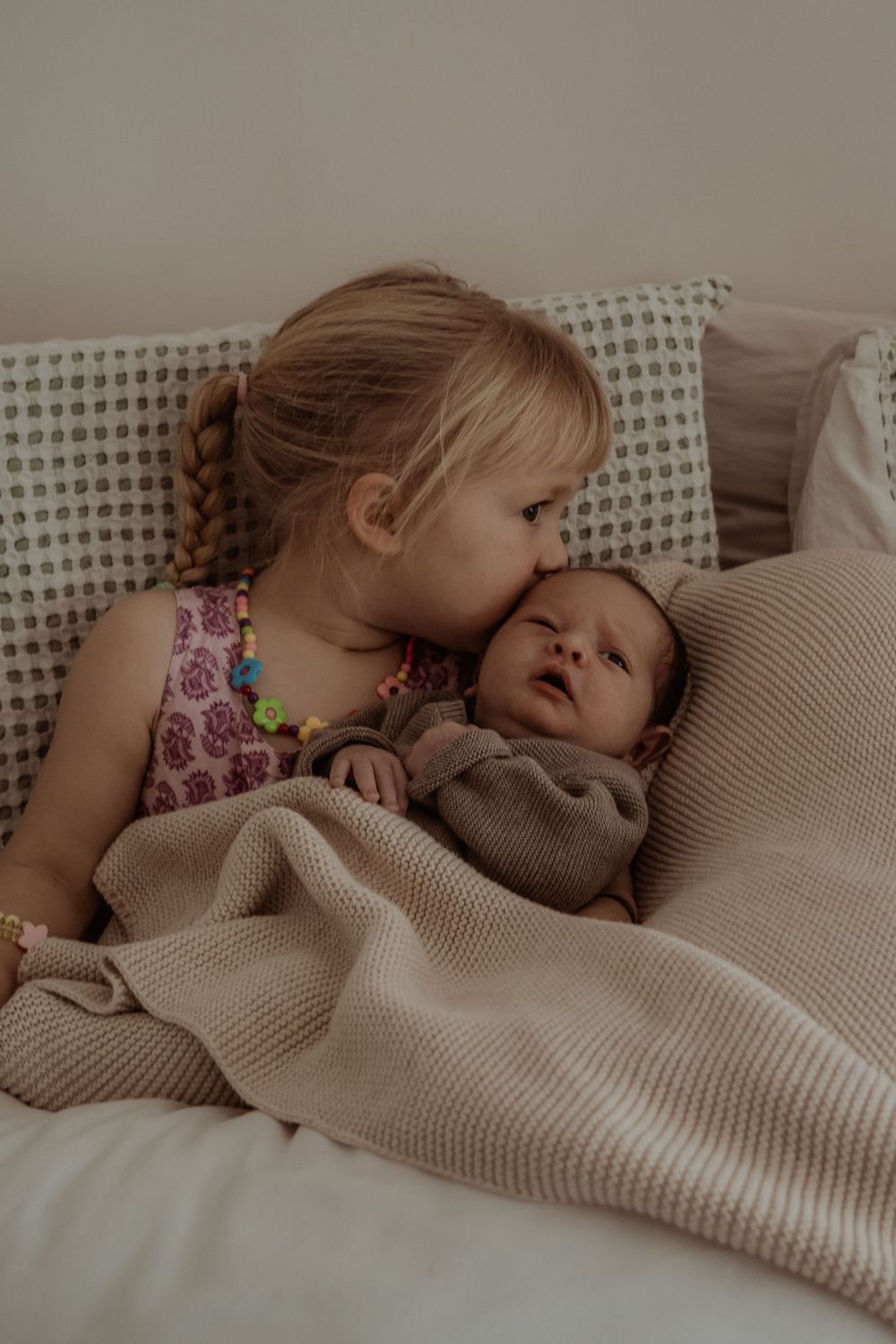 Two siblings cuddling together under knit blanket during quiet moment during a central coast newborn photoshoot.