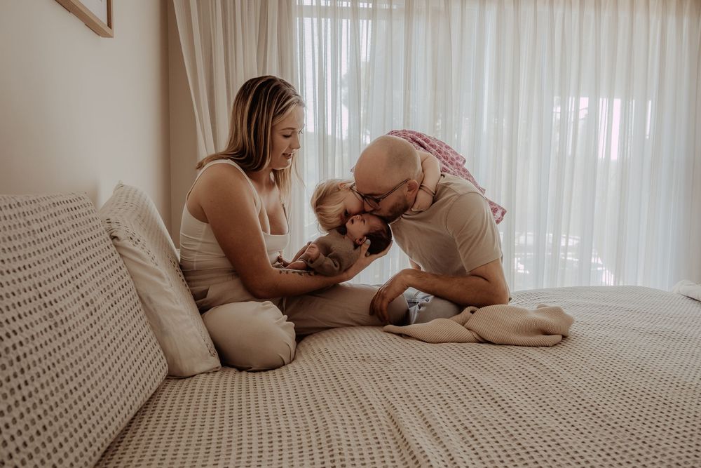 Intimate family portrait on bed with natural window light streaming through sheer curtains at a central coast newborn session.