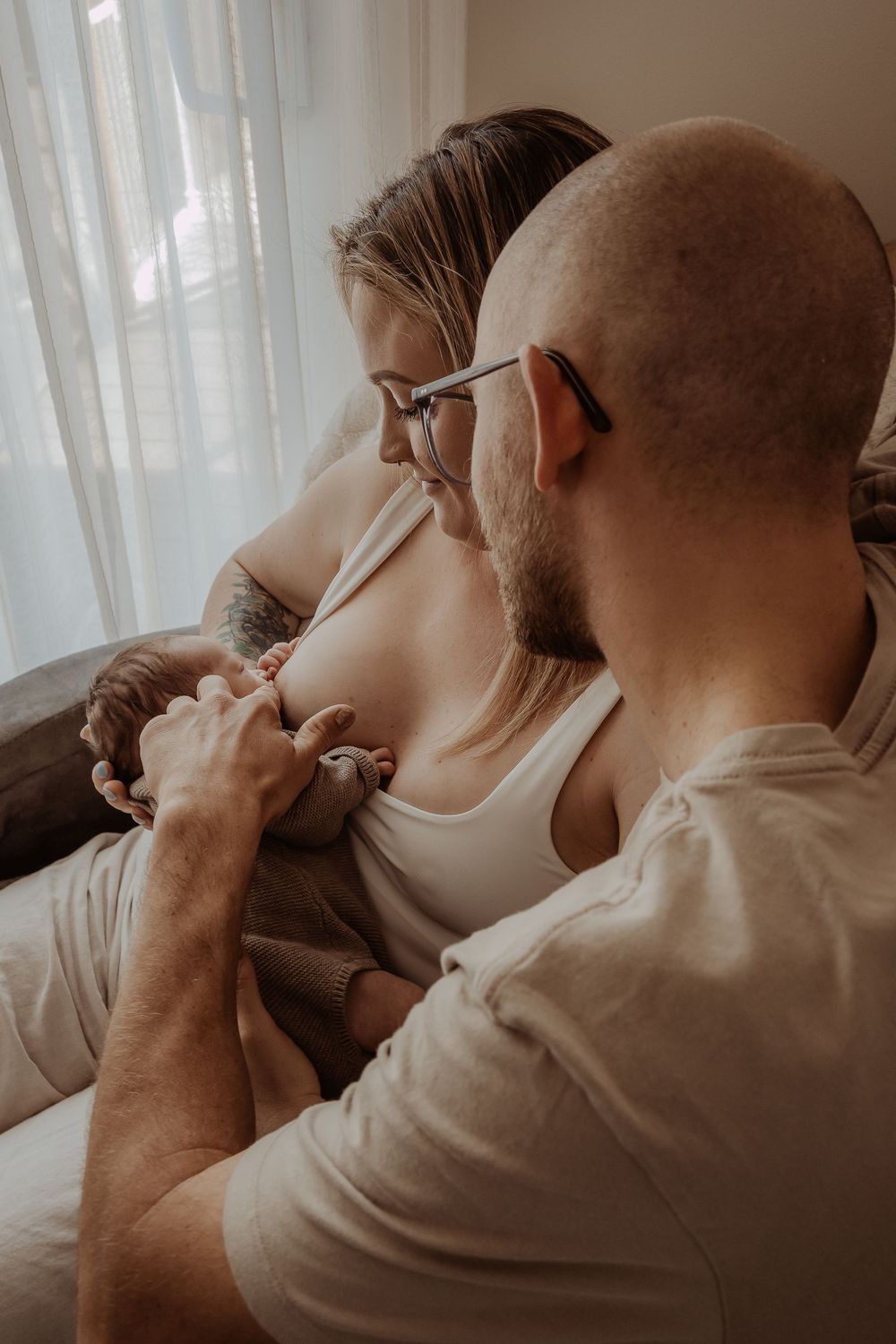Family sharing affectionate moment together near window with soft natural lighting during a central coast newborn photoshoot.