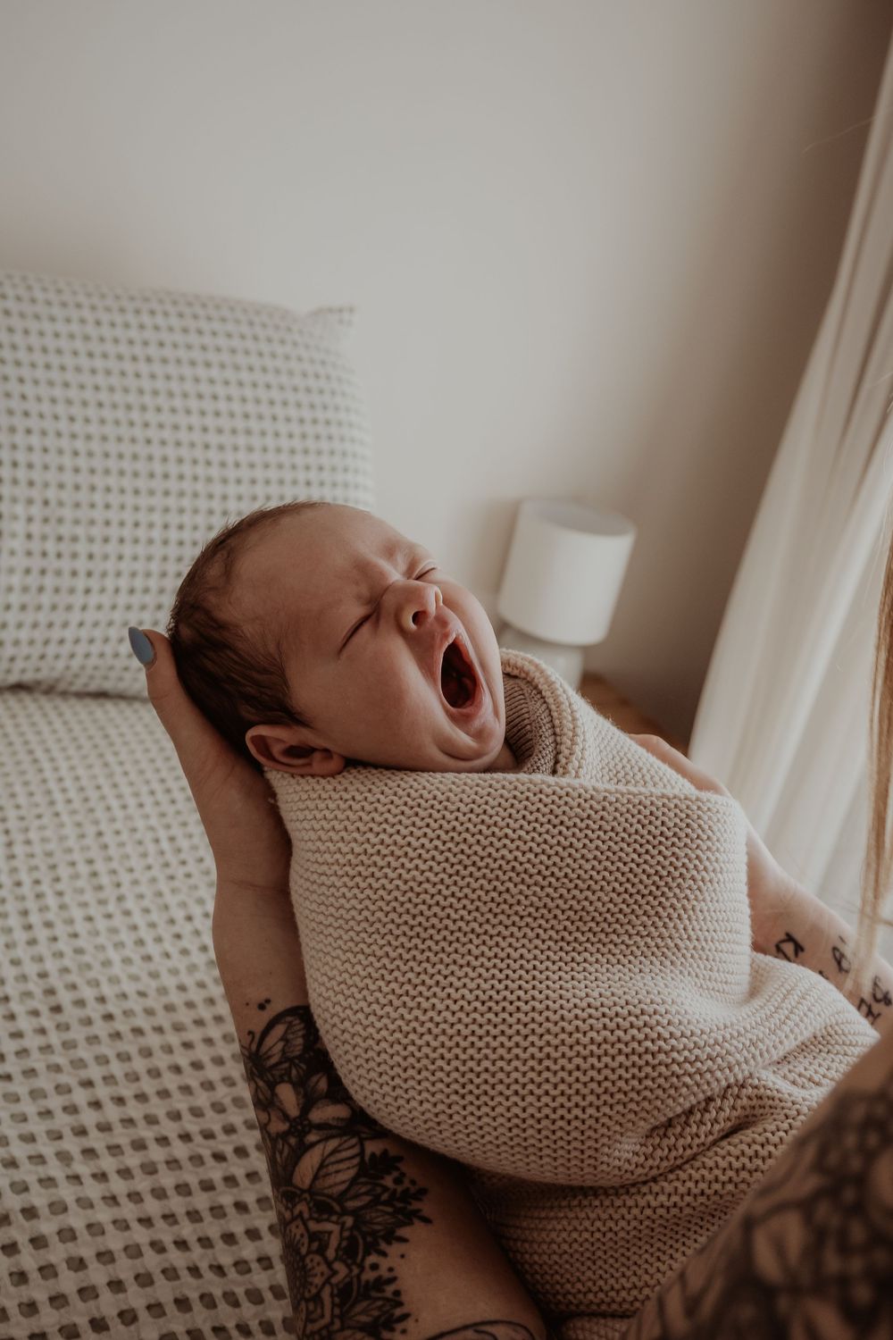 Yawning newborn baby wrapped in cozy knit blanket against neutral background during a central coast newborn photoshoot.