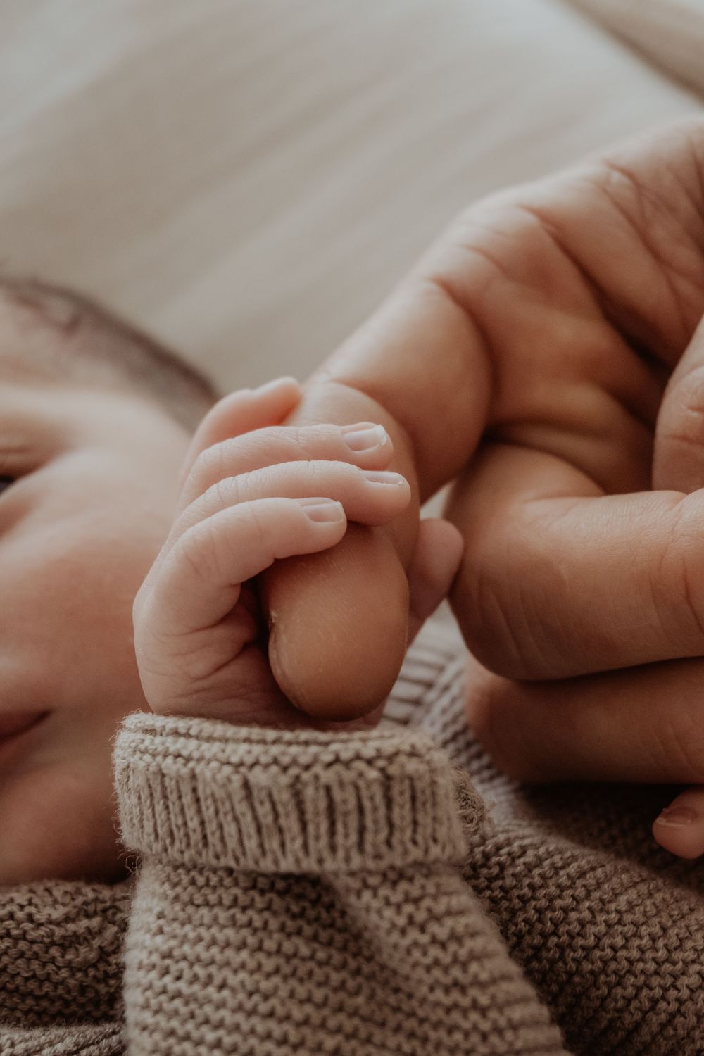 Close-up of tiny baby hands grasping his fathers finger in soft lighting during a central coast newborn photoshoot.