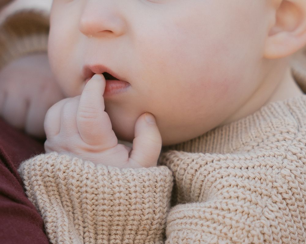 Close-up of someone wearing a cozy cream knit sweater while touching their face in a gentle pose.