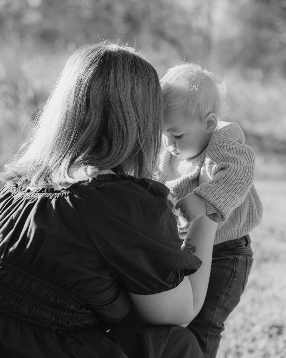 A series of black and white photos showing tender moments between a young child and someone with long hair outdoors.