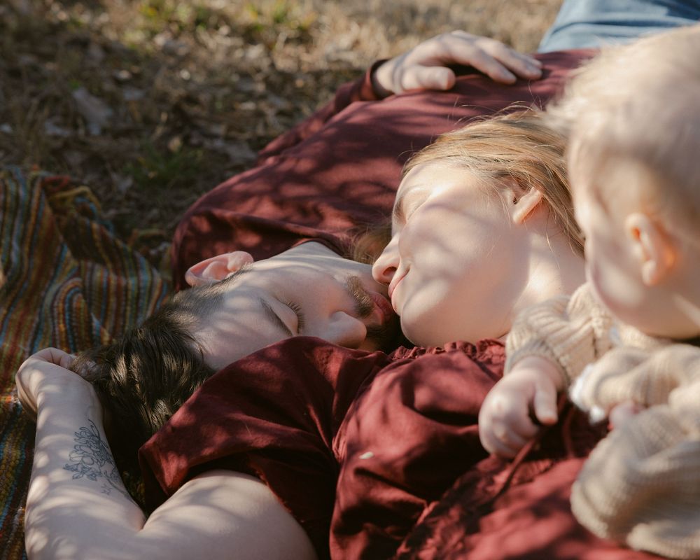 Three people lying down together on the ground in burgundy clothing during golden hour sunlight.