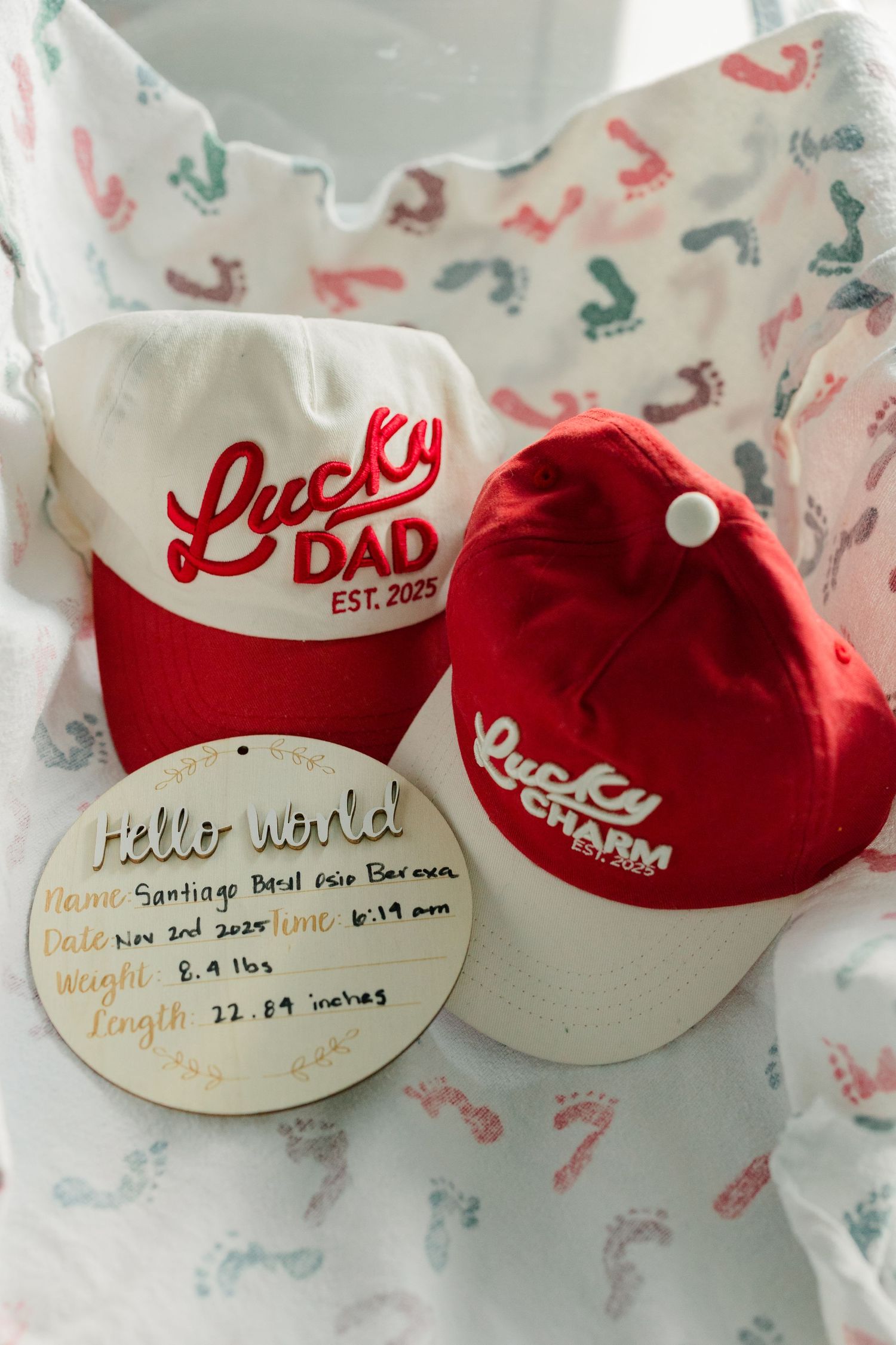 Two red and white 'Lucky Dad' baseball caps with birth announcement details written on a round card.