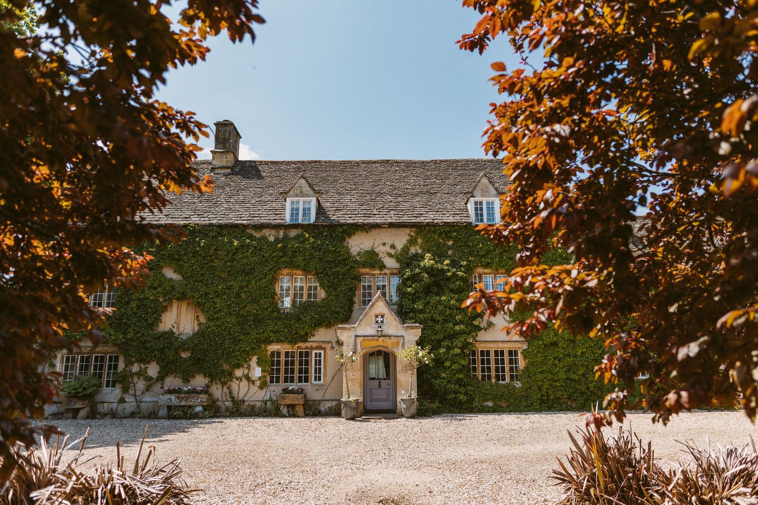 Historic stone manor house with ivy covered walls and autumn trees framing the view on a sunny day.