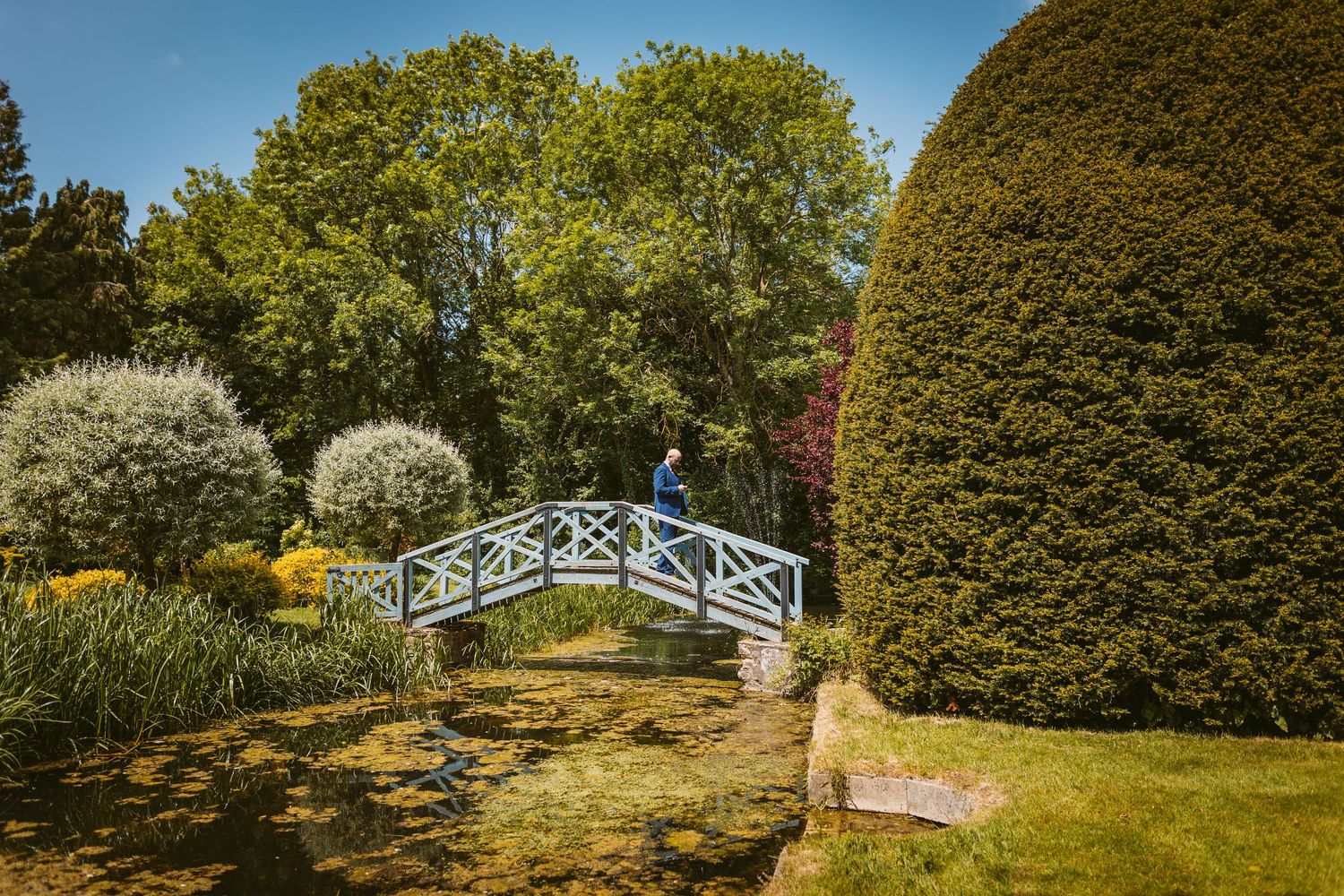 A series of garden pathways and bridges winding through lush greenery and manicured hedges in a formal garden setting.