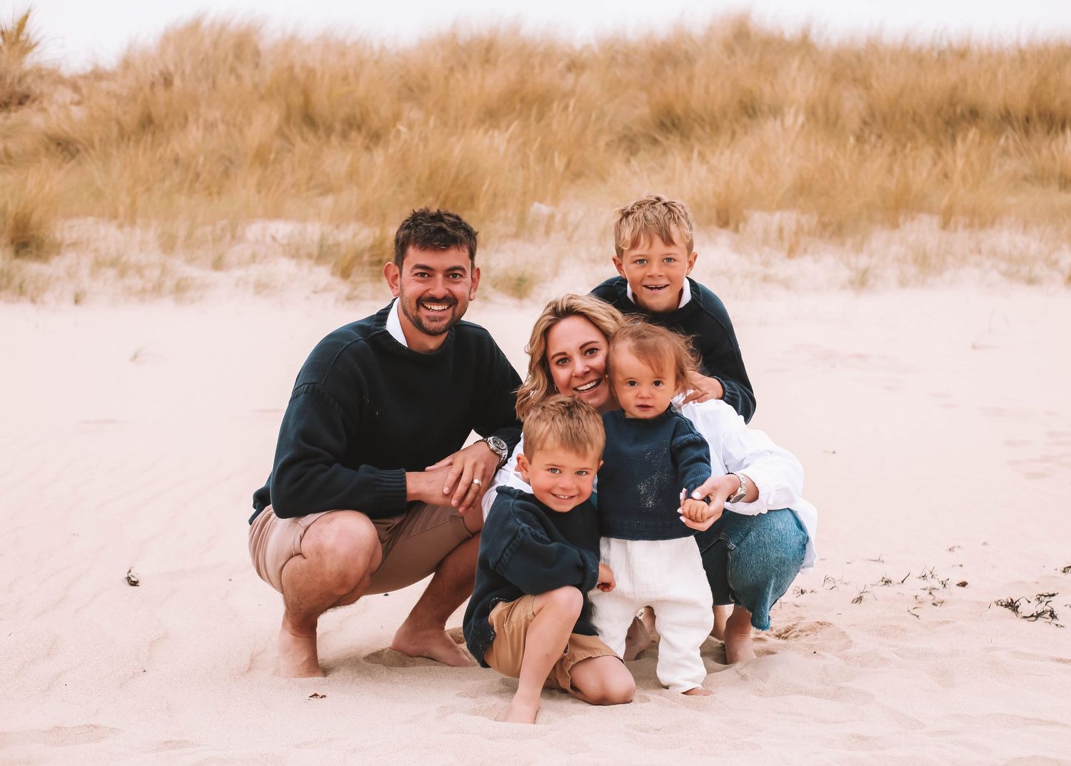A family enjoys a playful moment together lying in the sand at the beach during sunset.