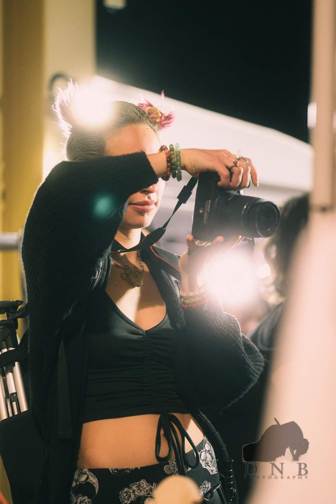 A female photographer raises her camera to capture a shot amid bright studio lights.