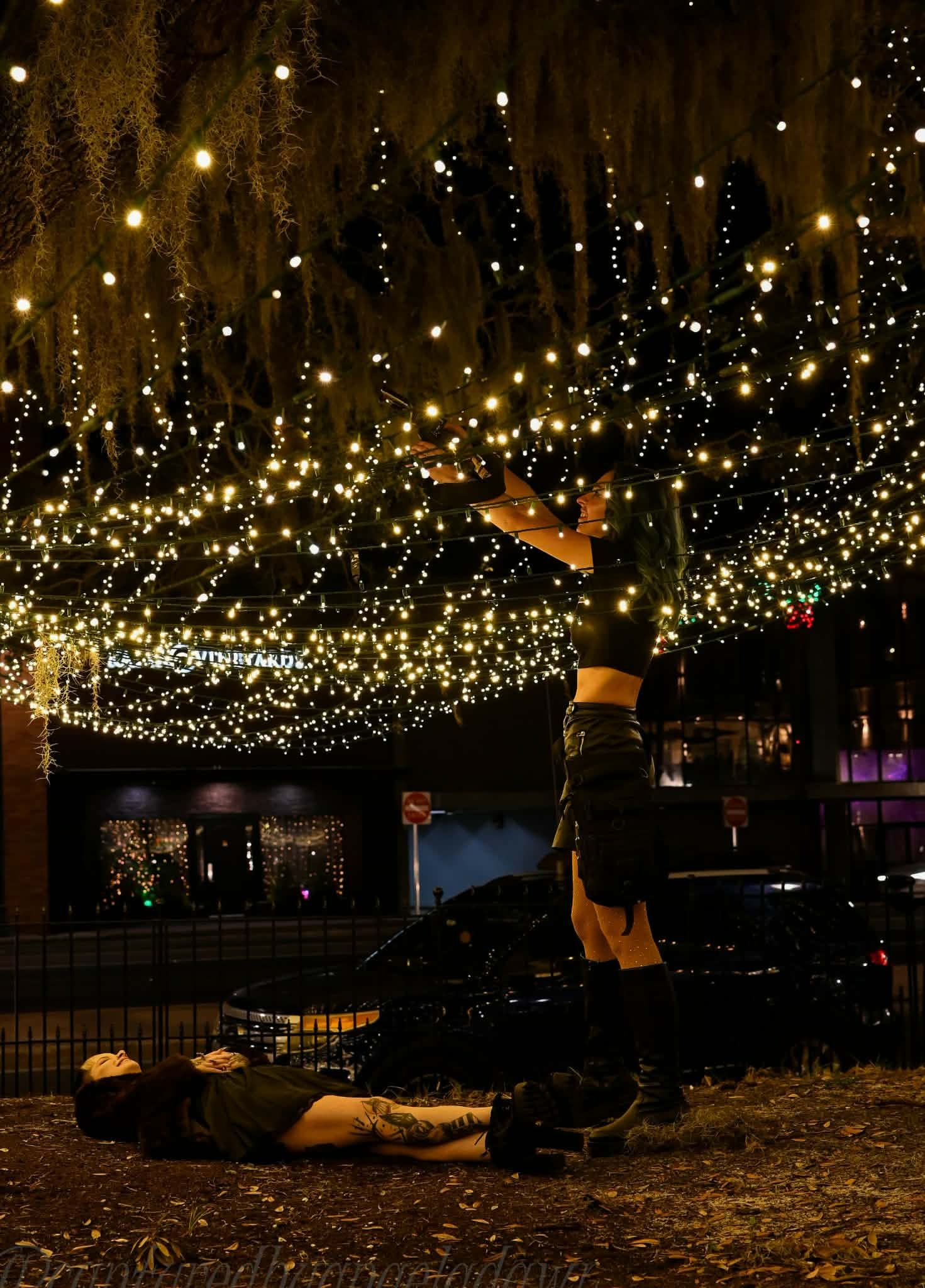 A person does a headstand under a canopy of warm twinkling lights at night.