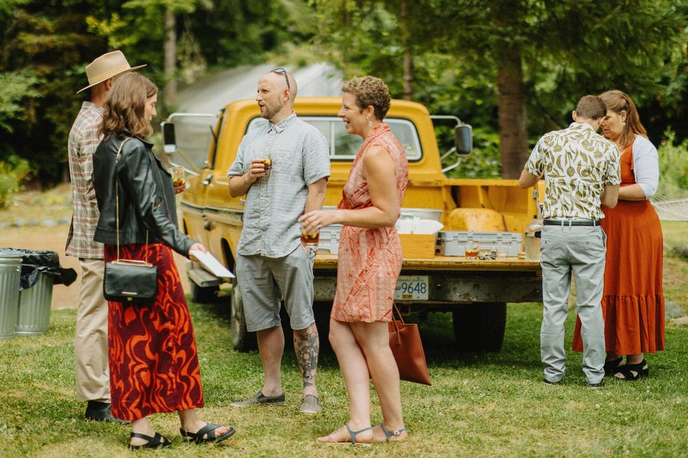 Wedding guests mingle and celebrate at an outdoor reception with wooden tables and chairs.