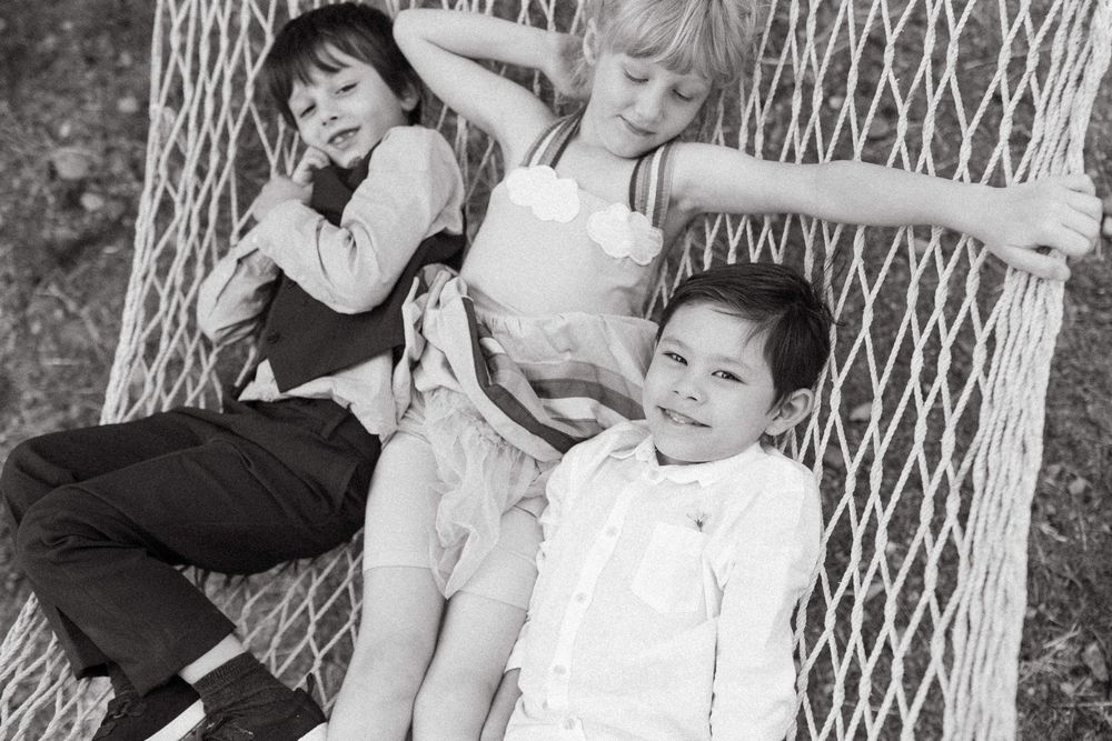 A vintage black and white photo of children relaxing in a hammock together.
