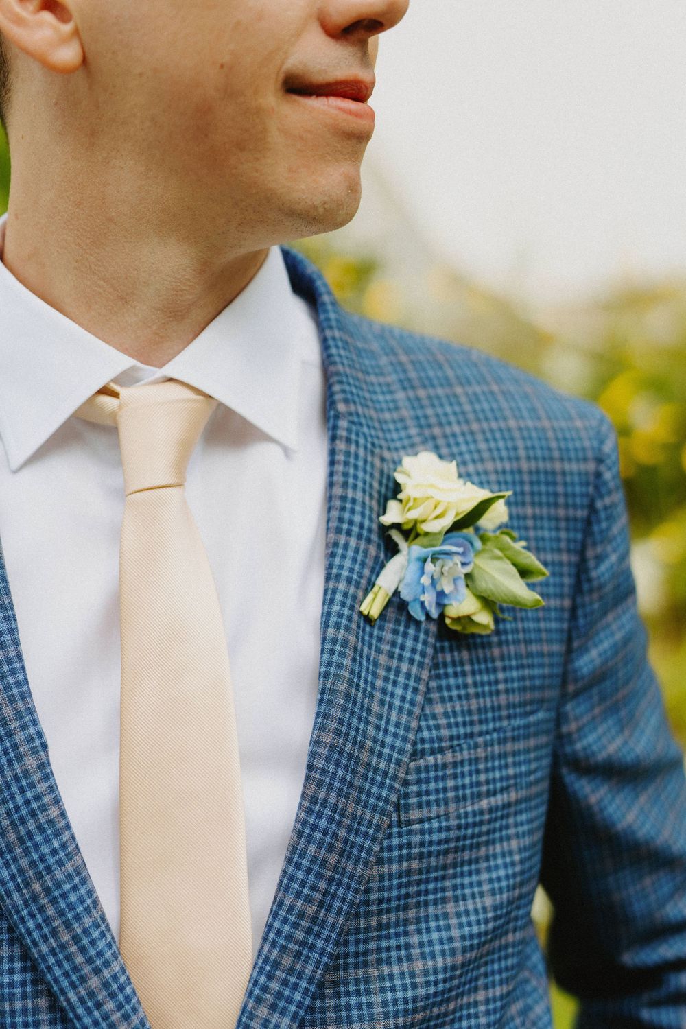 Close-up details of a blue checkered suit jacket with cream tie and white boutonniere.