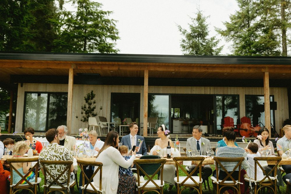Wedding reception guests seated at long tables on an outdoor covered patio.