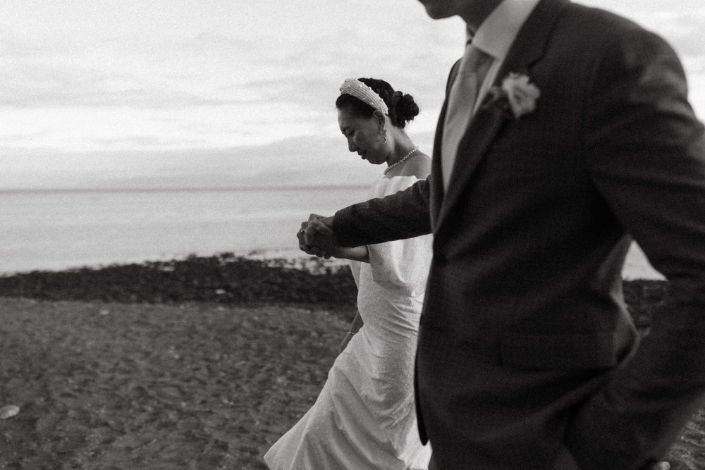 A romantic black and white photo of a couple walking on a beach during their wedding day.