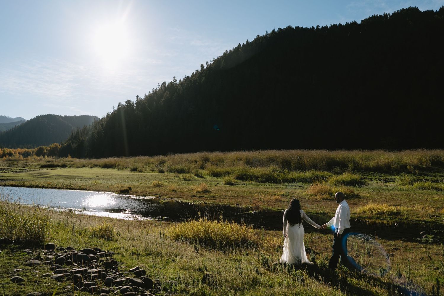 A scenic mountain meadow with a winding river and forest-covered hills under golden sunlight.