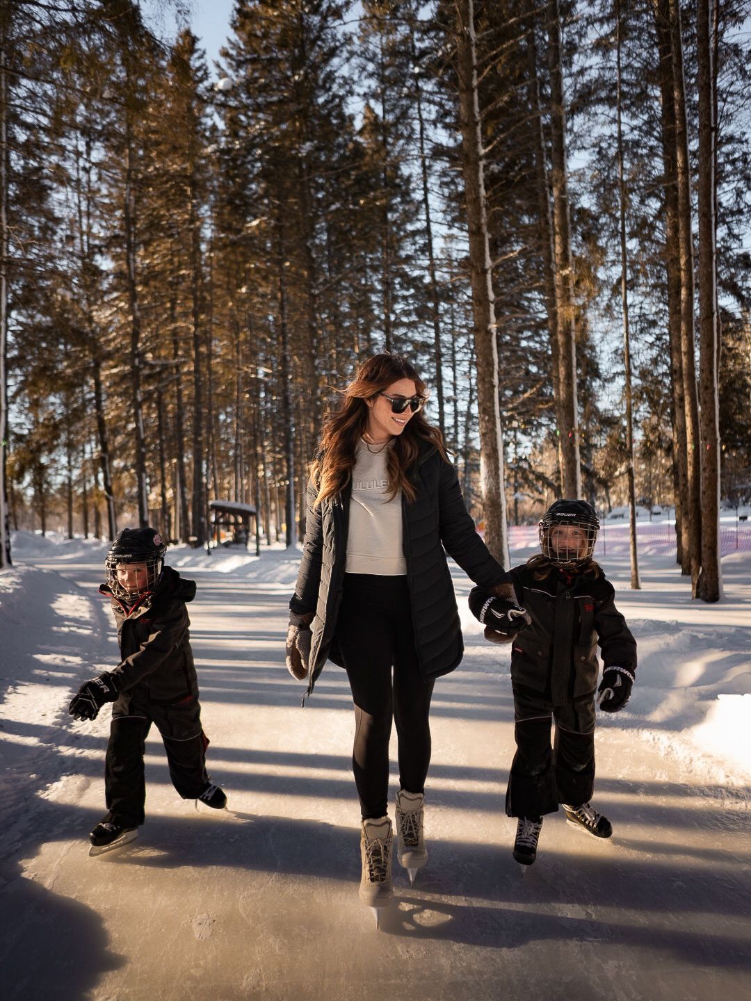 Winter scene showing people walking through a snowy forest path at sunset.
