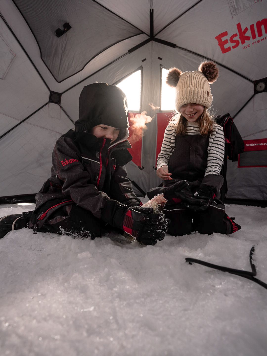 People ice fishing inside a red portable shelter on frozen lake.