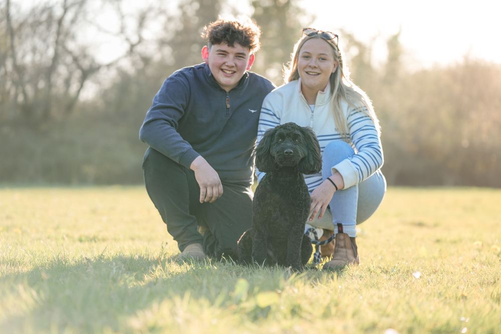 Couple sitting in grass field with their black dog during sunset.