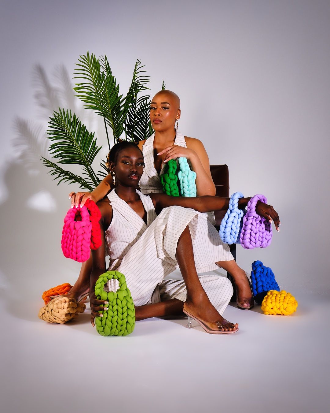 Studio portrait with models displaying collection of vibrant knitted handbags.